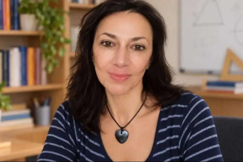 учителка с тъмно синя блуза на бели линии зад нея бяла дъска и рафт с книги